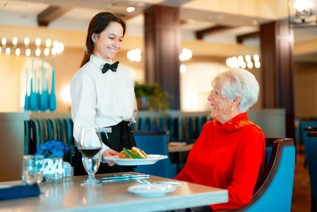Waitress serving food to a woman in a red sweater.