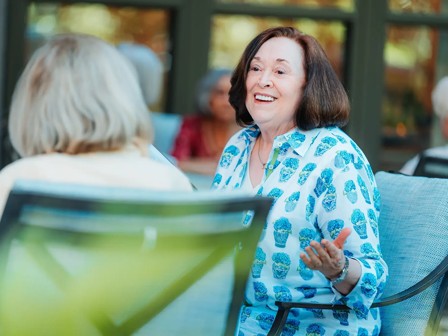 Woman in blue top sitting outdoors conversing with friends.