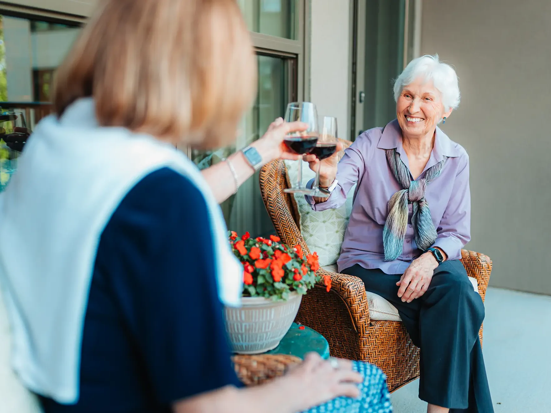Two ladies sitting on porch "cheers-ing" wine glasses.