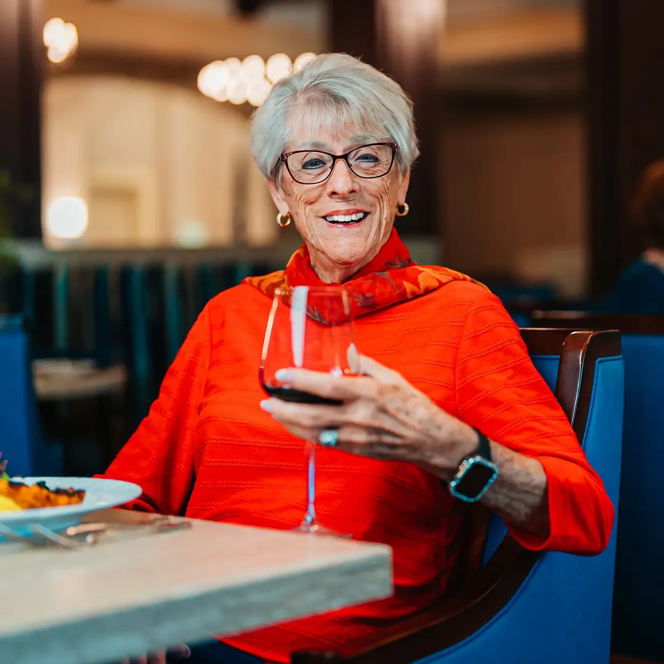 Legacy Pointe resident in bright red sweater holding a glass of wine.