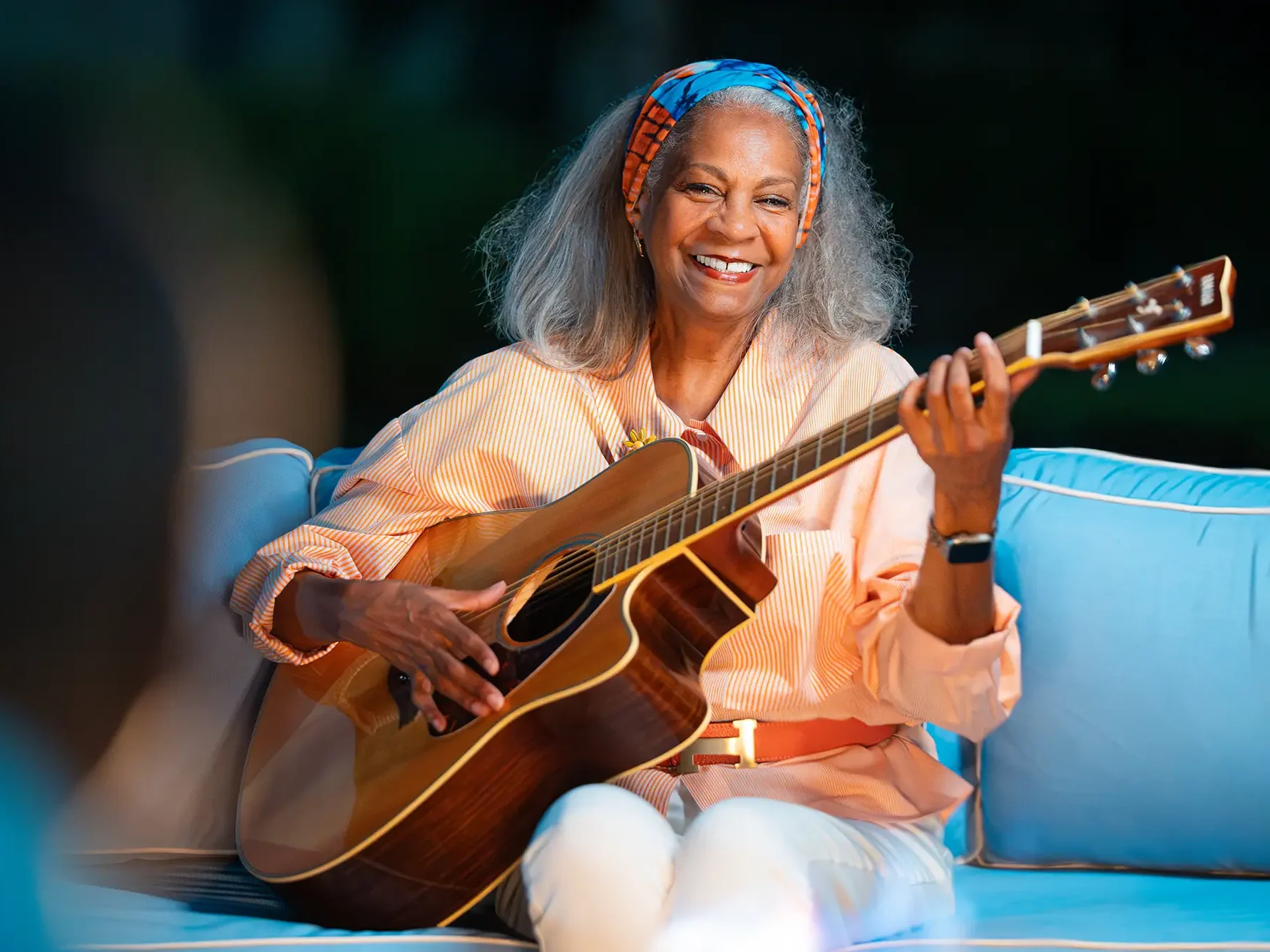Woman sitting outside playing guitar.