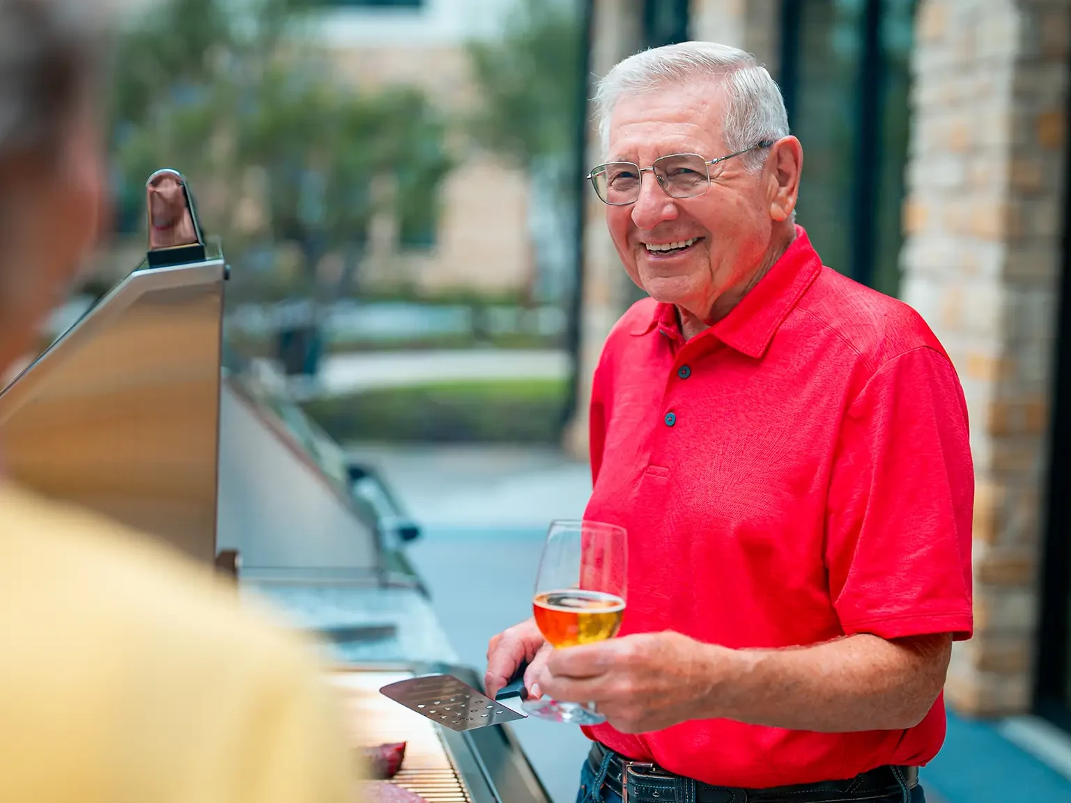 Resident at grill holding spatula and a beer glass.