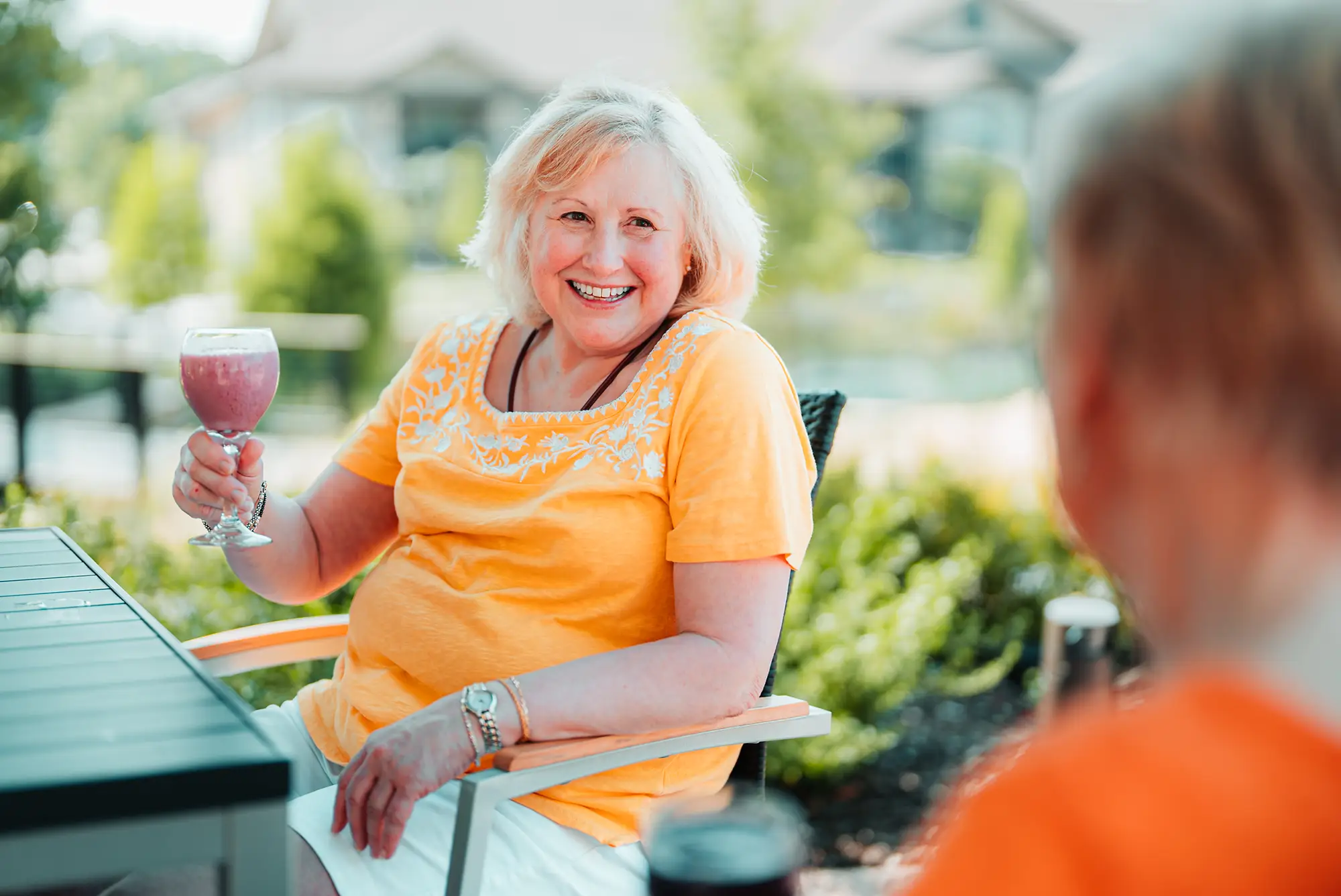 Woman in yellow top seated on a patio raising a glass of pink wine.