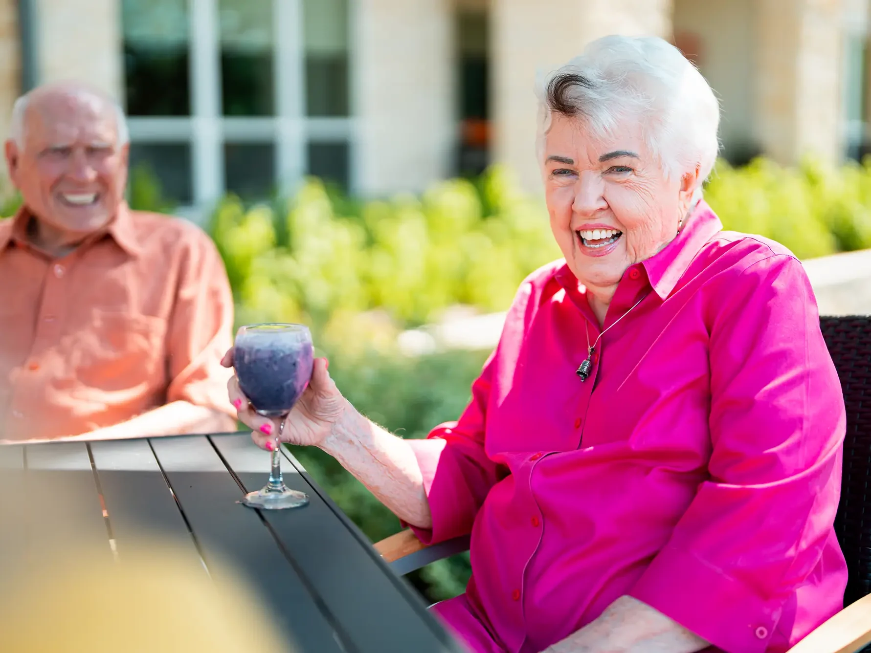 Woman in bright pink shirt sitting at a patio table with friends drinking a glass of wine.