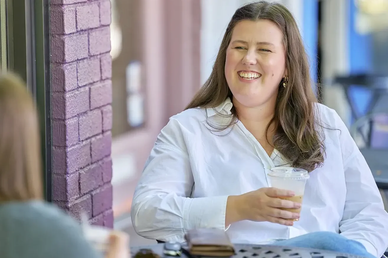 Employee at a cafe table, outside of work, smiling.