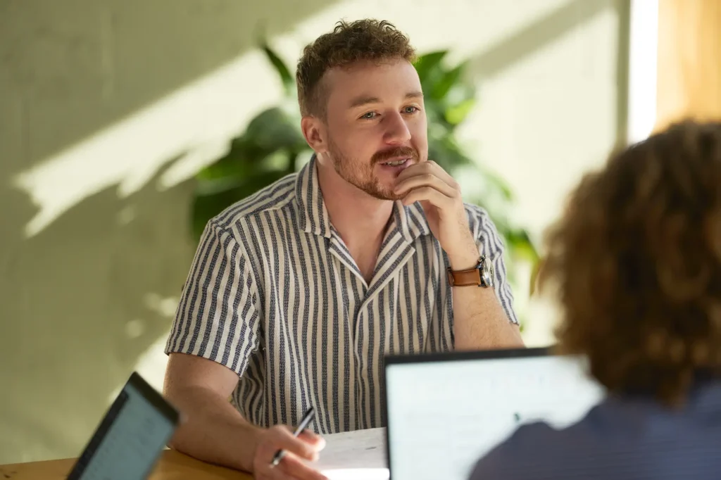 Employee in meeting, touching his chin in contemplation.