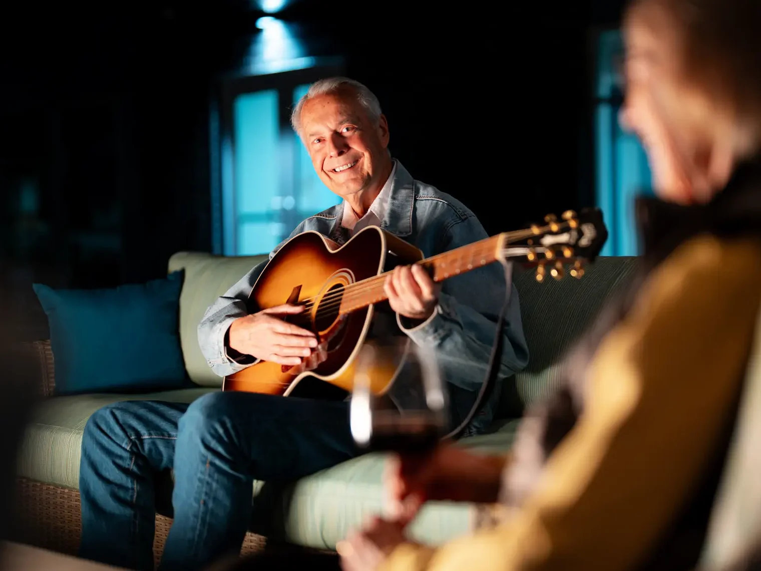 Man seated on patio, playing a guitar by the fire pit.